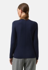 Granatowy top z długim rękawem, okrągłym dekoltem i centralnym szwem z tyłu, zestawiony z jasnoszarymi, wzorzystymi spodniami.