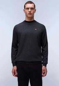 Jersey de cuello redondo gris oscuro hecho de un tejido suave. Cuenta con mangas largas y un pequeño emblema rojo y blanco en el pecho.