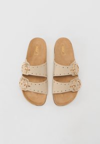 Sandales à glissière beiges avec deux larges brides, boucles en métal doré, accents à clous et semelle intérieure rembourrée couleur tan. Design à semelle plate.