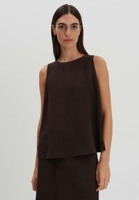 Top marrone senza maniche in lino, con una vestibilità rilassata, scollo rotondo e una texture liscia. Indossato con una gonna coordinata.