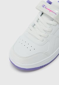 Λευκό αθλητικό παπούτσι με διάτρητη μύτη, κορδόνια, μοβ εξωτερική σόλα και ασημένιο λουράκι με την επιγραφή "Champion". Υλικό από λείο δέρμα.