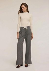 Lichtbeige geribbelde trui met hoge hals, gecombineerd met losse grijze joggingbroek met zijopeningen en een witte trekkoord. Bruine schoenen met hak.