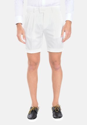 Pantaloni corti bianchi plissettati con risvolti, abbinati a scarpe nere con lacci gialli. Il materiale sembra liscio, leggero e casual.