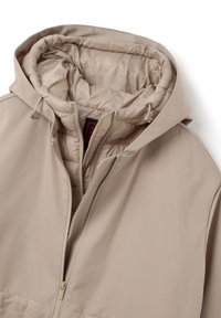 Giacca beige con cappuccio, dotata di un esterno liscio, chiusura con zip e imbottitura trapuntata. Presenta cordini regolabili e un'etichetta con il marchio all'interno.