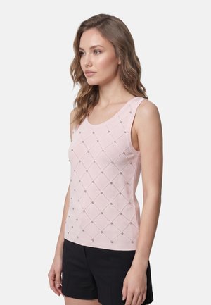 Femme aux cheveux ondulés portant un haut sans manches rose clair avec de petits détails en perles en motif losange et un short noir.