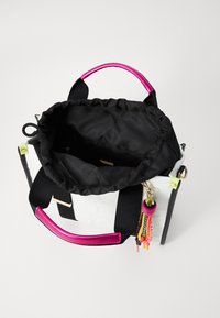 Weiße und schwarze Handtasche mit pinken Griffen, schwarzem Innenraum, gerafftem oberen Teil und bunten Quastenakzenten. Aus robustem Stoff mit minimales Design.