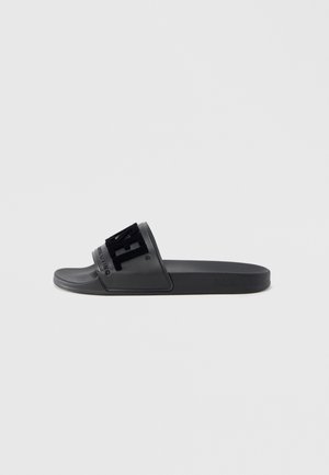 Sort gummiglide-sandal med en bred rem, der har hævet sort tekst. Flad sål og glat tekstur. Minimalistisk design.