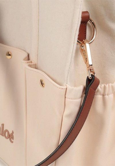 Borsa in tela con esterno beige chiaro, dettagli in pelle e accessori dorati. Presenta tasche esterne e una tracolla removibile.