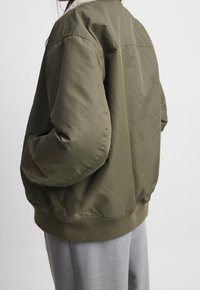 Cazadora bomber verde oliva con un suave cuello de color crema; presenta un material exterior liso y puños y dobladillo acanalados.
