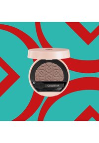 Compact d'ombre à paupières Collistar avec une teinte marron clair texturée, un boîtier extérieur rose et un applicateur noir, présenté sur un fond turquoise et rouge.