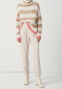 Stickad tröja med beige och vita ränder, med hög hals och rosa detaljer. Matchad med ljusbeiga byxor och vita ankelstövlar.