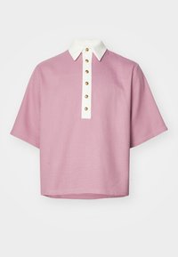 Rövid ujjú pólóing rózsaszín színben, texturált mintázattal, fehér gallérral és arany gombokkal az elején. Hétköznapi, laza fazon.