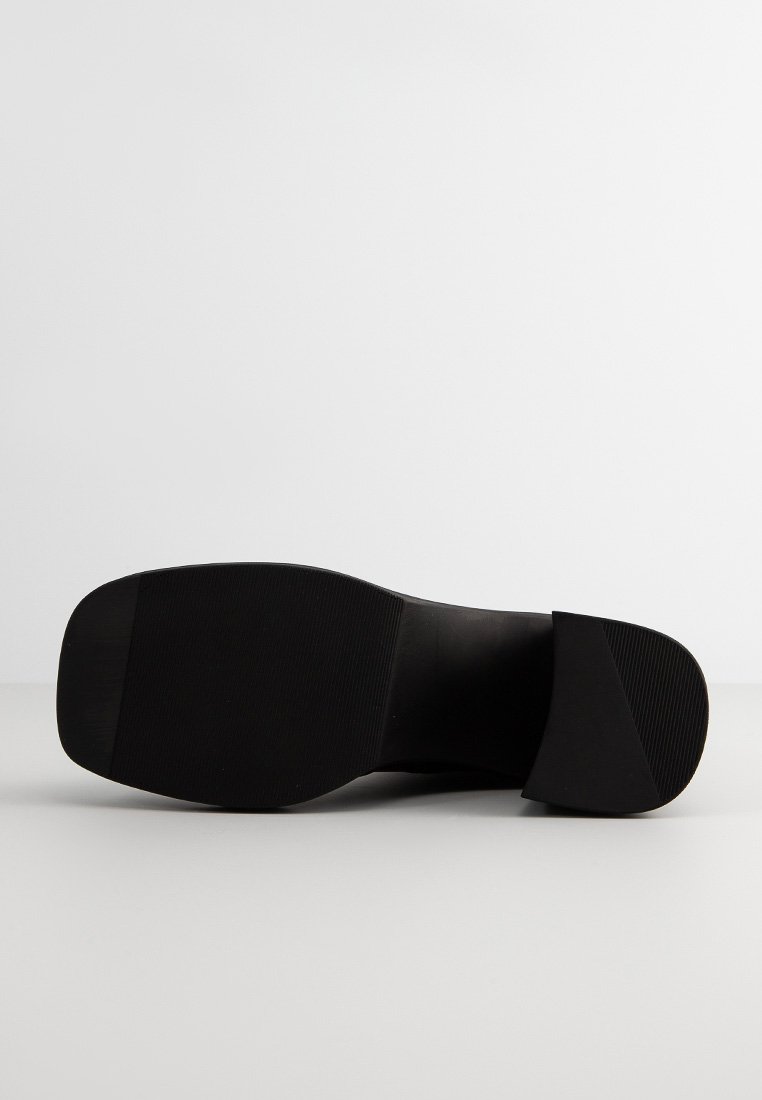 Semelle de chaussure en caoutchouc noir avec une surface texturée ; design plat, bout légèrement arrondi et sans marques ou accents visibles.