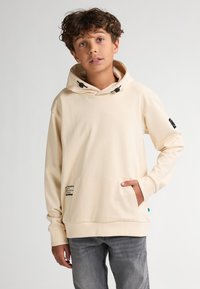 Sudadera con capucha beige hecha de un tejido suave, que presenta un bolsillo delantero y un cordón ajustable. Incluye una pequeña etiqueta gráfica en el lateral.