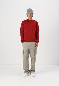 Punainen crewneck-huppari, beige cargo-housut taskuilla, harmaa lippalakki ja valkoiset lenkkarit. Yksinkertainen muotoilu, rento kangasrakennetta ja rento istuvuus.