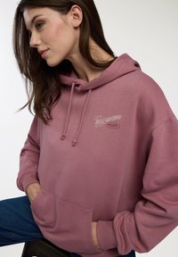 Felpa con cappuccio rosa realizzata in morbido tessuto, con tasca frontale, coulisse regolabile e logo ricamato sul petto.