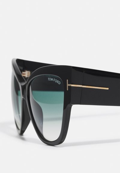 Sorte oversized solbriller med gradientlinser, utstyrt med en gullmetallaktsent på stangen og "TOM FORD" merkevare i hvitt.