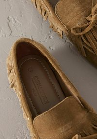 Mocassini in suede marrone con dettagli a frange, suola piatta e accenti cuciti. Interno etichettato con "SIGNATURE" e informazioni sulla taglia.