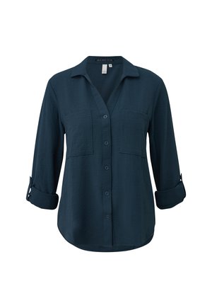 Donkerblauw overhemd met lange mouwen, knopen en twee borstzakken, met opgerolde mouwen tot halverwege de onderarm.