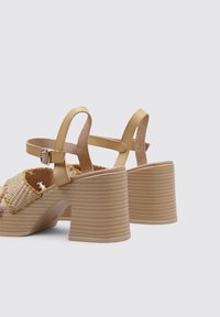 High-heeled sandals with a gold strap, woven beige upper, and textured light brown platform. Features a buckle on the ankle strap.