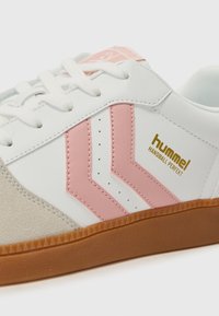 Sneaker bianco con chevron rosa e marchio dorato. Presenta una punta in suede beige testurizzato, lati perforati e suola in gomma color ocra.