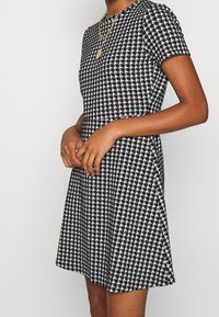 Kortärmad klänning i svart och vitt hundtandsmönster, med utsvängd kjol, tillverkad av textiler, med rund halsringning och figurnära liv.