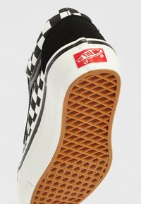 Baskets de skate en damier noir et blanc avec une semelle blanche proéminente, présentant un fond en caoutchouc texturé avec un motif en nid d'abeille et un logo rouge.