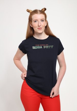 Mørkeblå t-shirt med korte, rullede ærmer, der har teksten "THE BOOK OF BOBA FETT" i røde og grønne skrifttyper. Båret med røde bukser.