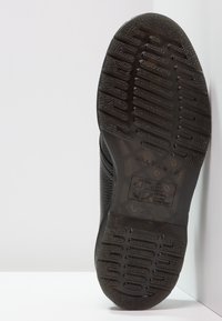 Semelle en caoutchouc noir avec motif antidérapant texturé et finition lisse. Côté avec une tige en cuir à motif. Logo visible sur la semelle.