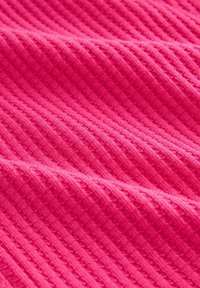 Helles pink gemustertes Stoffmaterial mit einem gerippten Muster, das erhöhte Linien und ein weiches, gewebtes Erscheinungsbild aufweist.
