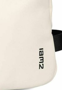 Lichtbeige tas van glad materiaal, voorzien van een zwart gedrukt "iamz" logo en een contrasterende zwarte schouderband. Rond bentuk.