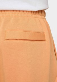 Jogger de algodón melocotón con cinturilla elástica, que presenta un bolsillo trasero en forma de rectángulo, con una textura suave.