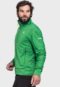 Grüne Outdoor-Jacke mit hohem Kragen, glatter Textur und Reißverschlusstaschen. Verfügt über ein Logo und kontrastierende Designelemente an den Ärmeln.