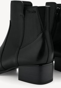 Schwarze Leder-Stiefeletten mit glatter Textur, ausgestattet mit einem Blockabsatz, elastischen Seiteneinsätzen und einem dezenten Logodetail an der Außenseite.