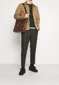 Brun skjortjacka över en mörkgrön tröja, olivfärgade byxor och svarta snörskor. Brun lädermessenger bag med silverdetaljer.