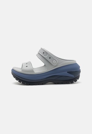 Lysegrå sandal med justerbar hælrem, kraftig blå mellemsål og sort robust sål, vist fra siden på hvid baggrund.