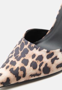 Παπούτσι mule με μυτερή μύτη, μπεζ και μαύρο λεοπάρ ύφασμα στο πάνω μέρος και μαύρη εσωτερική επένδυση.