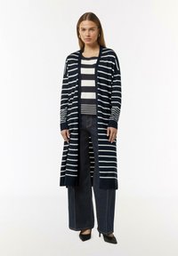 Navy- und weiße gestreifte lange Strickjacke mit offener Front, langen Ärmeln und gerippten Bündchen, kombiniert mit einem gestreiften Oberteil und dunklen weit geschnittenen Jeans.