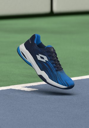 Blue and black sports shoe with white sole hovering above a tennis court surface near the boundary line.