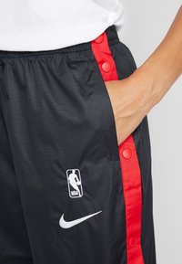 Czarne sportowe szorty z czerwonymi zatrzaskami, ozdobione logo Nike i emblematem NBA, wykonane z gładkiego, lekkiego materiału.