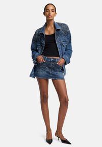 Giacca di jeans con dettagli in borchie, abbinata a un top nero e a una gonna di jeans coordinata. Caratterizzata da tessuto di jeans blu e da un design aderente.