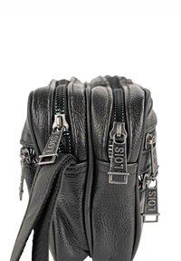 Bolso de piel negra con múltiples compartimentos, con cremalleras y herrajes plateados. Superficie texturizada con detalles de costura visibles.