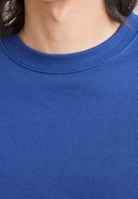 Camiseta de algodón azul con cuello redondo acanalado, textura suave y un diseño ajustado, que presenta un color sólido sin patrones visibles.