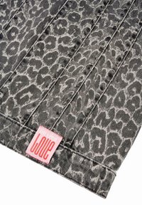 Svart og grå leopardmønstrete denimstoff, med vertikale sømmer og et rosa merke med ordet "KJÆRLIGHET" nederst.