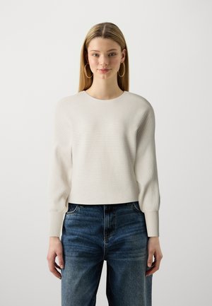 Light beige ribbed knit sweater with a round neckline and long, slightly puffed sleeves, paired with high-waisted blue jeans.
