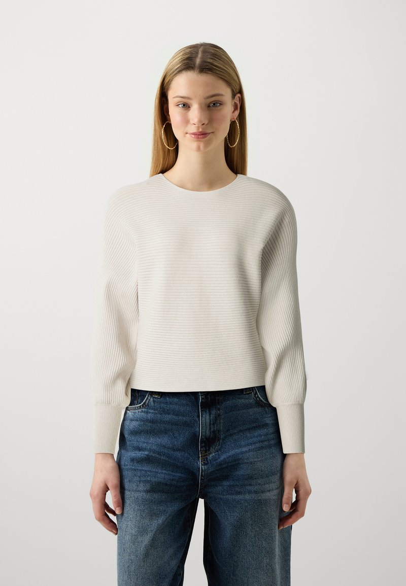 Light beige ribbed knit sweater with a round neckline and long, slightly puffed sleeves, paired with high-waisted blue jeans.