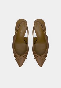 Καφέ γόβες slingback με μυτερή μύτη, μικρές κορδέλες και χρυσές αγκίστρες, προορισμένες να φαίνονται από πάνω σε λευκό φόντο.