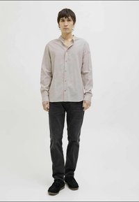 Camisa de botão de mangas longas em rosa claro com colarinho descontraído, combinada com jeans cinza escuro e sapatos pretos. Textura suave, design minimalista.