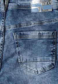 Jeans in denim blu chiaro con cuciture visibili, chiusura a zip e una tasca posteriore rettangolare con una leggera texture e effetti di scolorimento.