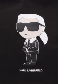 Cartoon character wearing oversized black sunglasses, white hair tied back, black suit, and white shirt. Text below reads "KARL LAGERFELD."